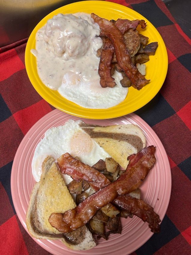 Two plates of food with eggs , bacon and gravy on a table.
