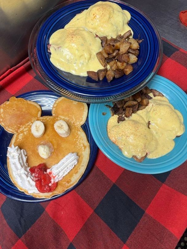 Three plates of food on a table including a pancake with a mickey mouse face on it