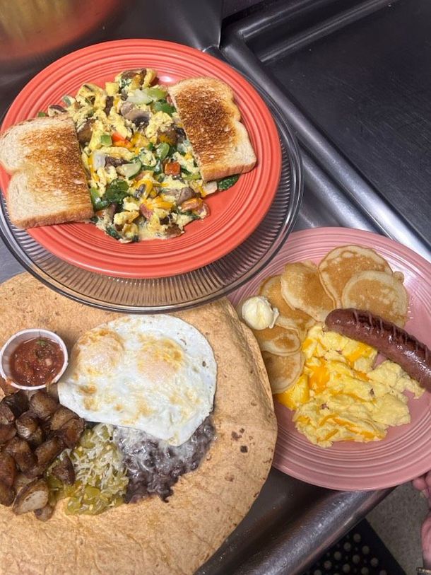 Three plates of food are on a counter including eggs pancakes and toast