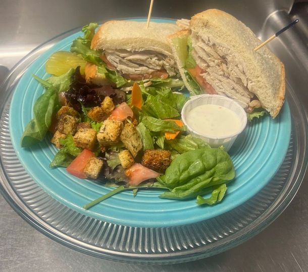 A blue plate topped with a turkey sandwich and a salad.