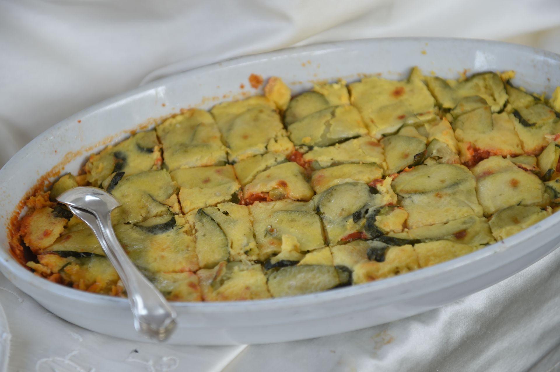 Una casseruola bianca piena di verdure e un cucchiaio d'argento.