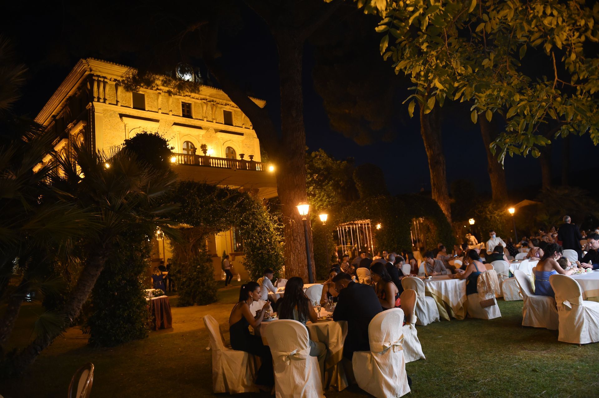 Un gruppo di persone è seduto ai tavoli davanti a un grande edificio di notte.