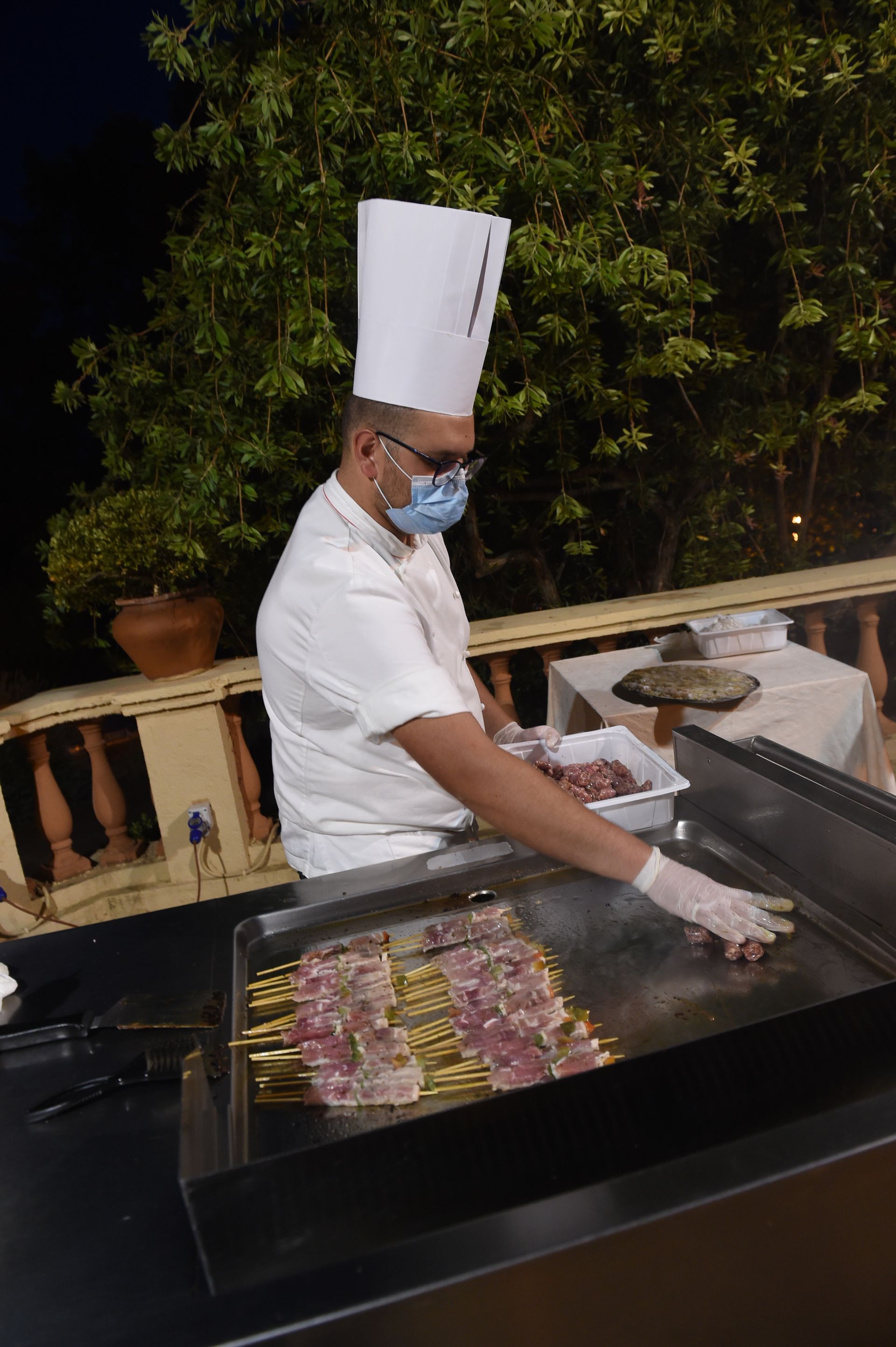 Uno chef che indossa una maschera e guanti sta cucinando il cibo su una griglia.