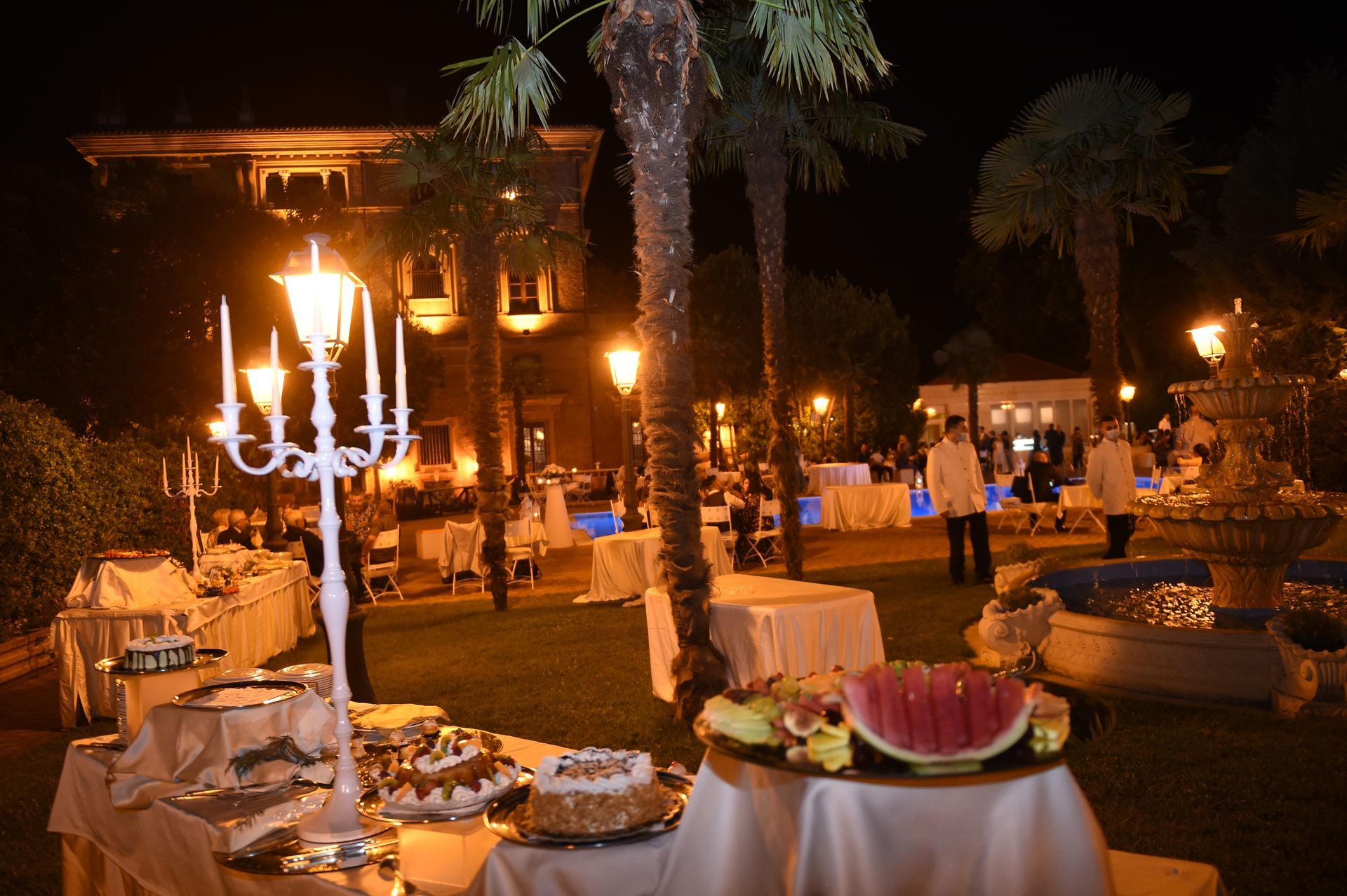 Un tavolo da buffet con candele e anguria sopra in un giardino di notte.
