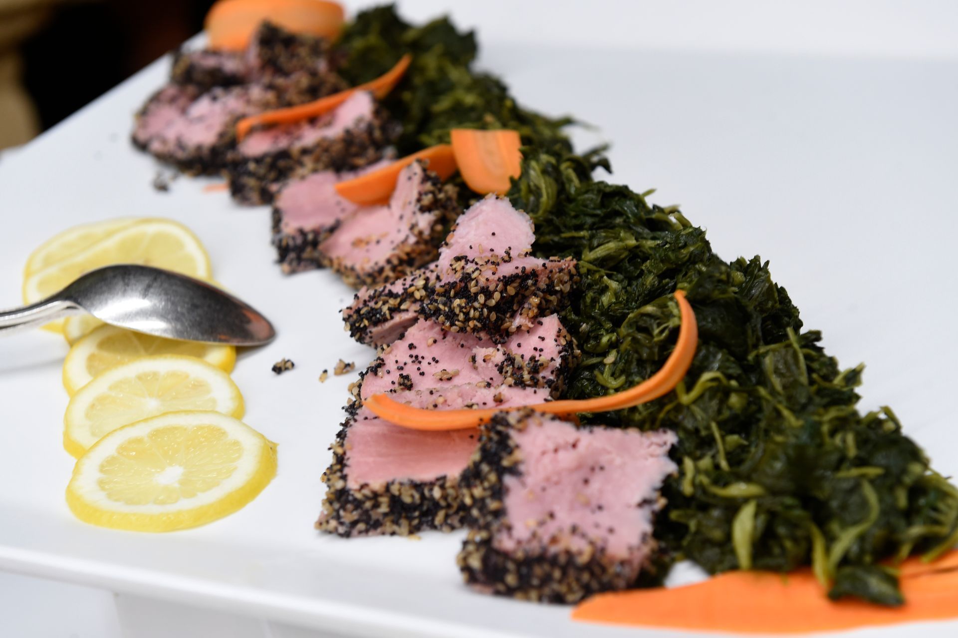 Un piatto bianco condito con carne, spinaci, carote e fette di limone.