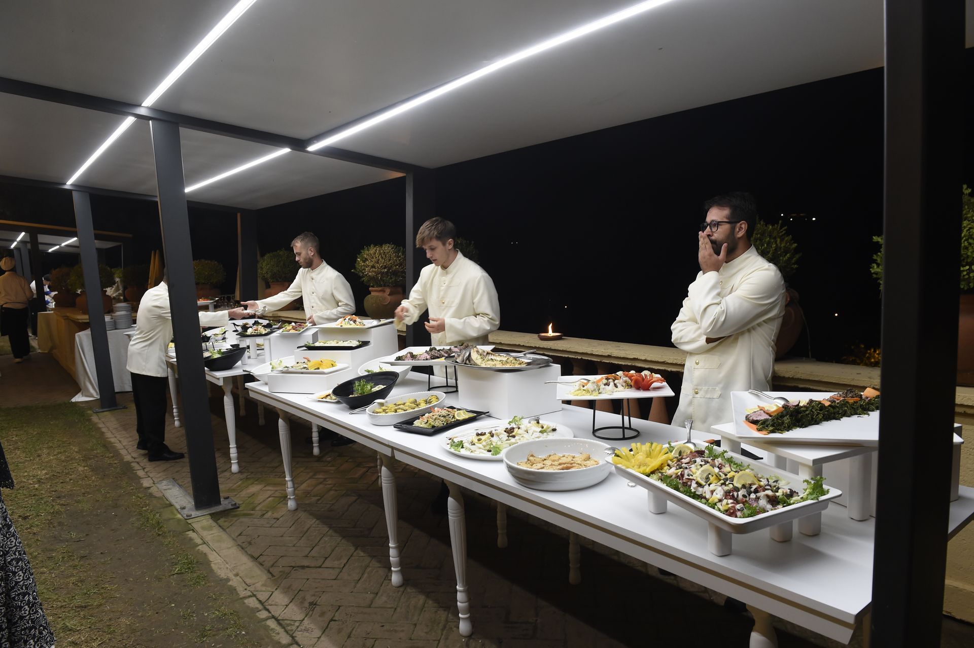 Un gruppo di uomini è in piedi attorno ad un lungo tavolo pieno di cibo.