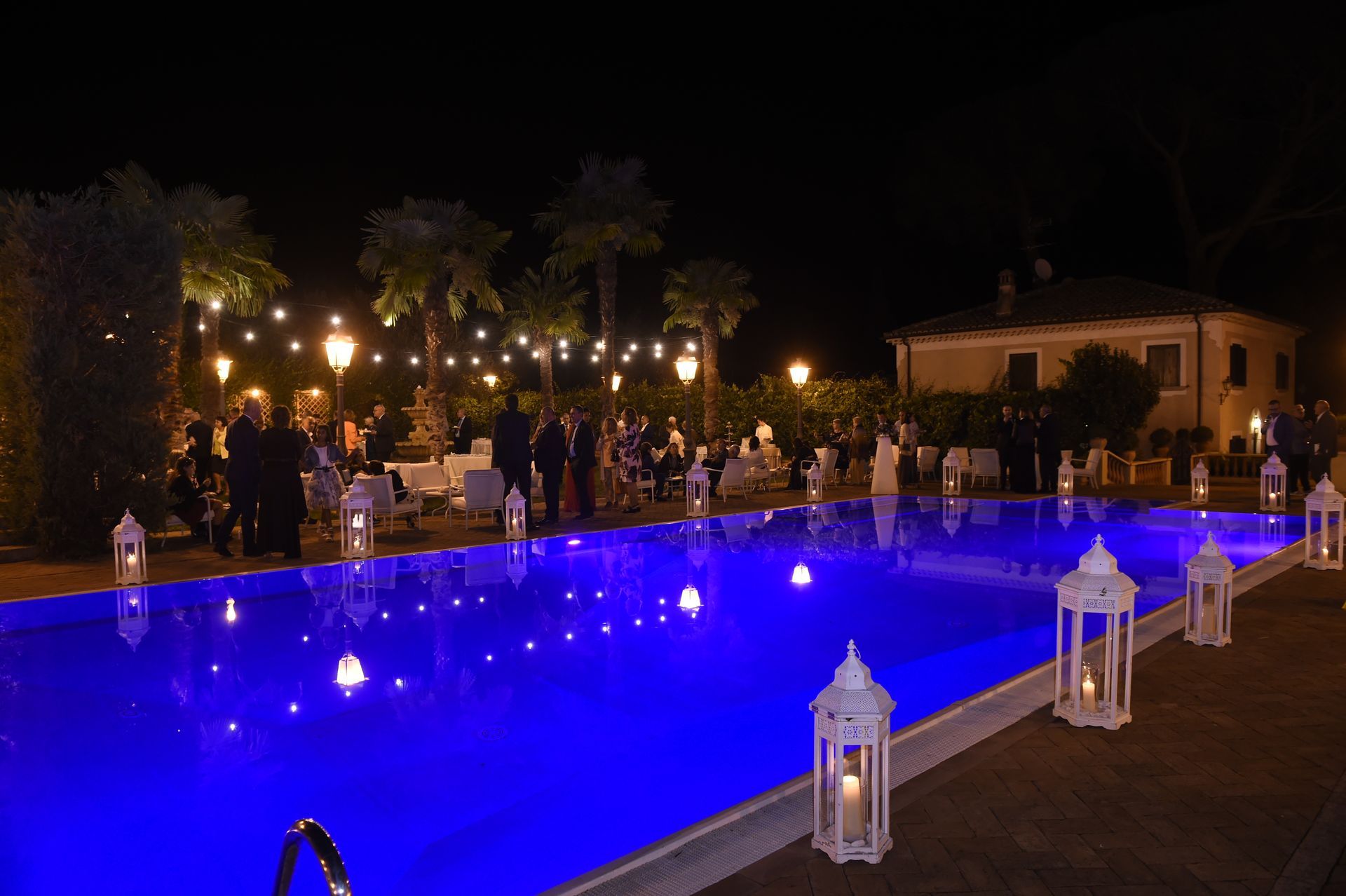 Una grande piscina è illuminata di notte con luci e lanterne blu.