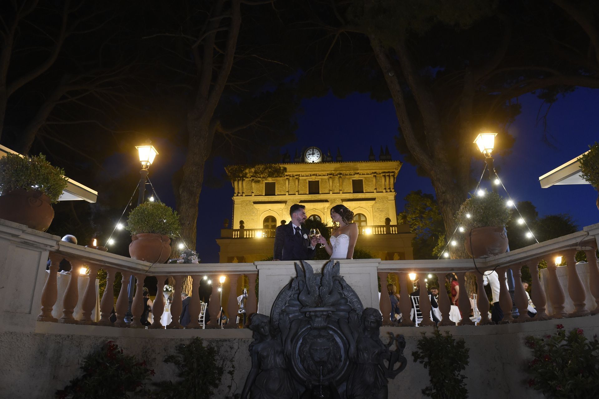 Una sposa e uno sposo sono in piedi su un balcone di fronte a un grande edificio di notte.