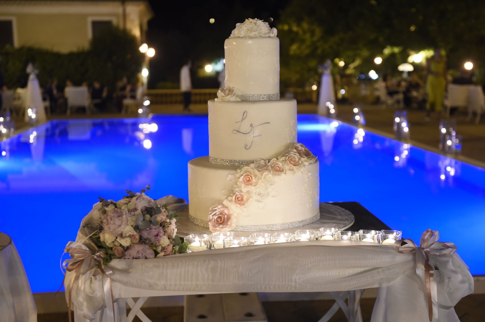Una torta nuziale è posata su un tavolo davanti a una piscina.
