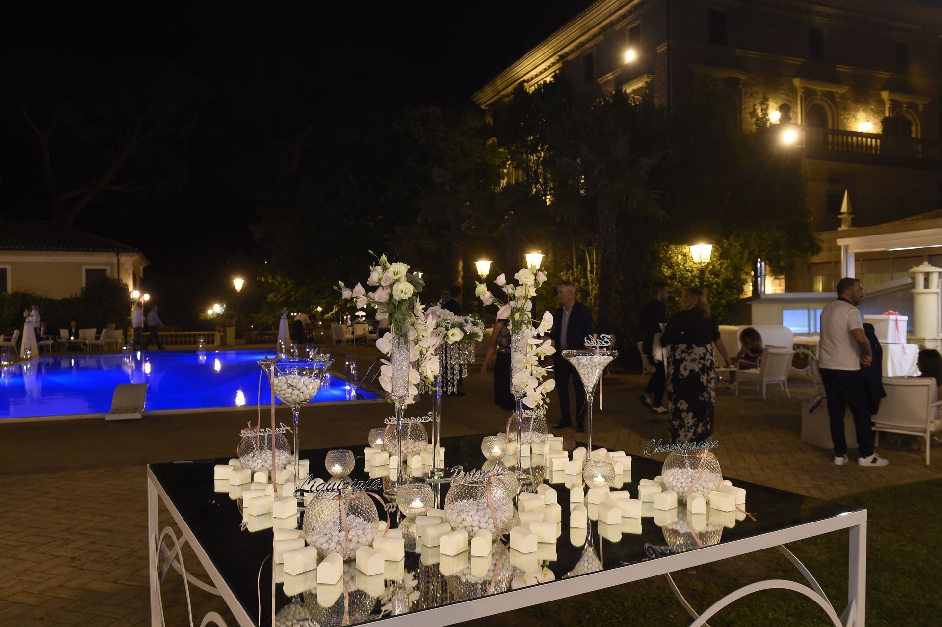 Un tavolo con candele e fiori davanti a una piscina di notte.