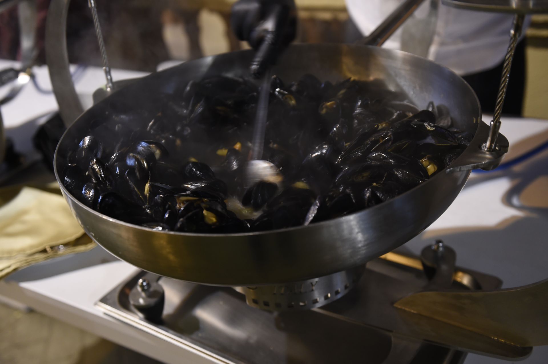 Una persona sta cucinando le cozze in una padella su un fornello