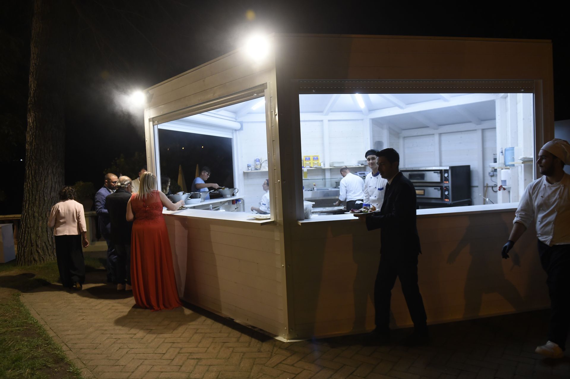 Di notte un gruppo di persone sta davanti a uno stand gastronomico.