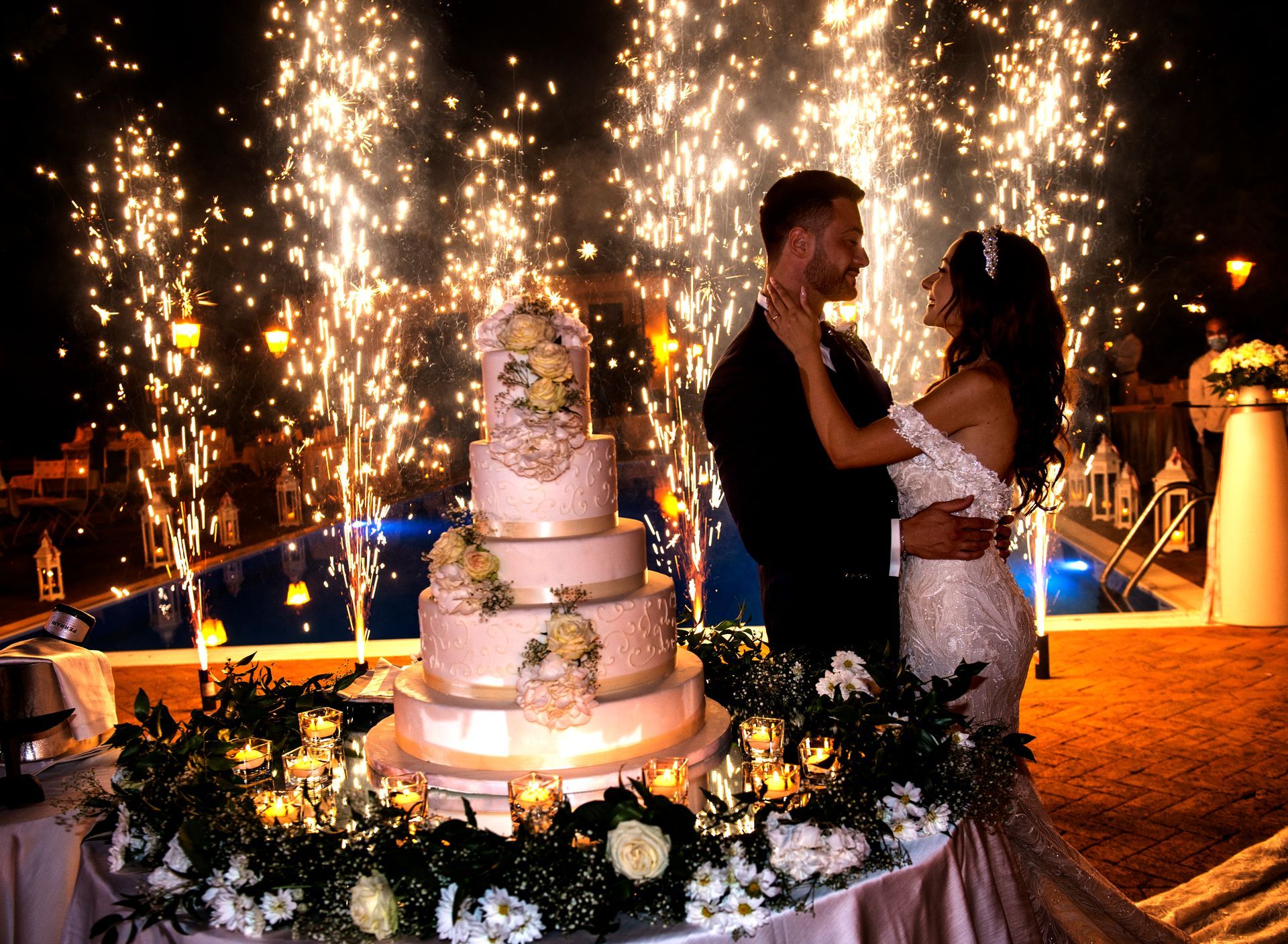 Una sposa e uno sposo sono in piedi davanti a una torta nuziale con fuochi d'artificio sullo sfondo.