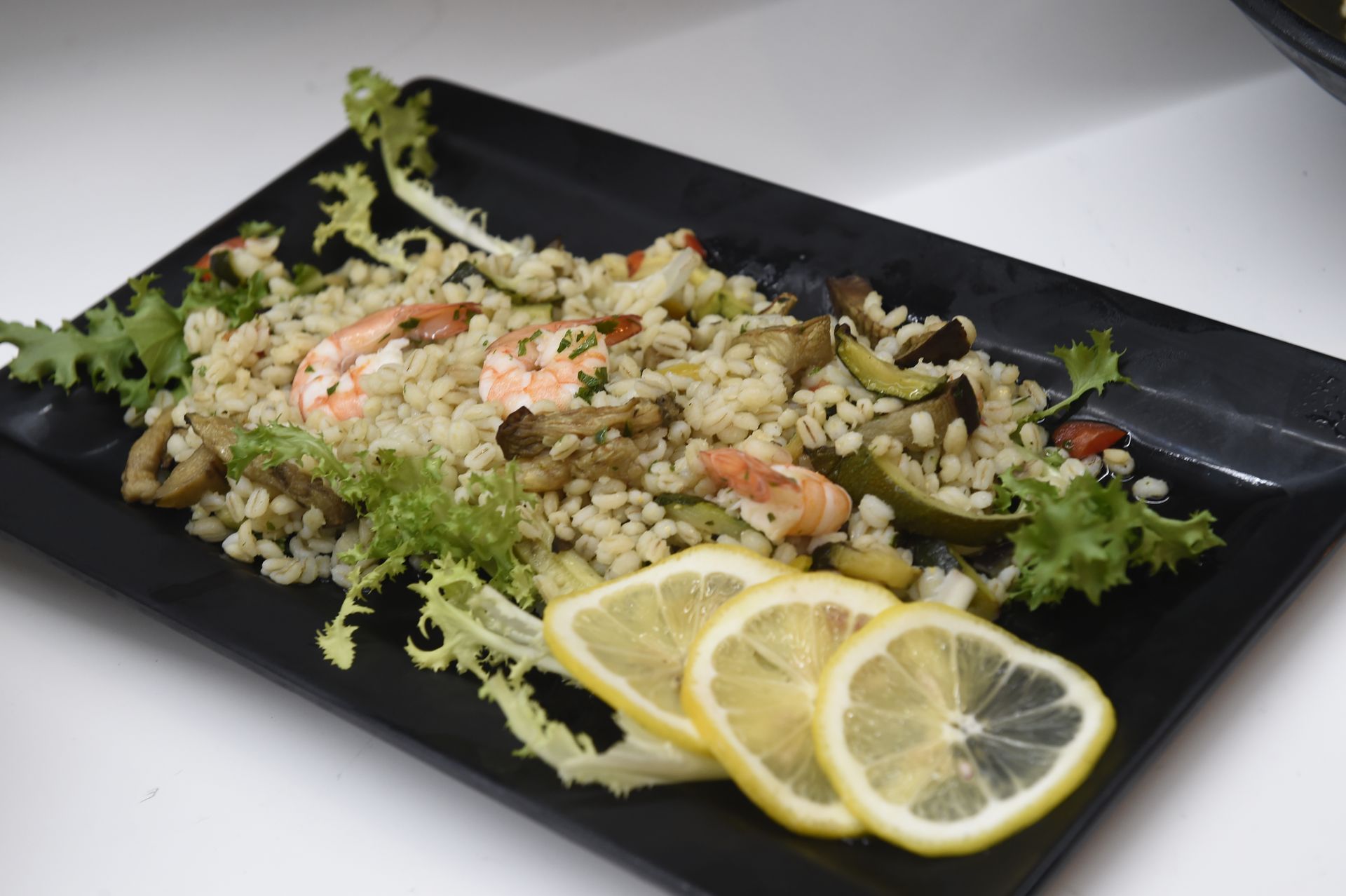 Un piatto nero condito con riso, gamberi e fette di limone.