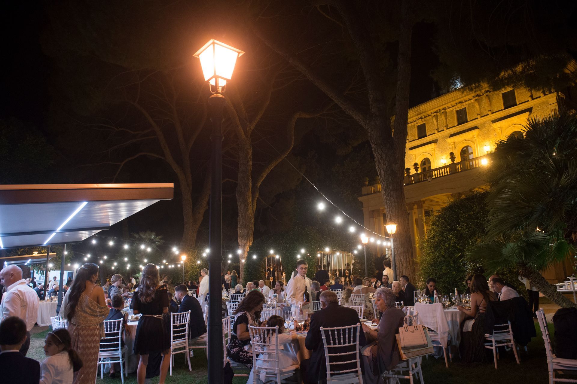 Di notte un folto gruppo di persone è seduto ai tavoli fuori.
