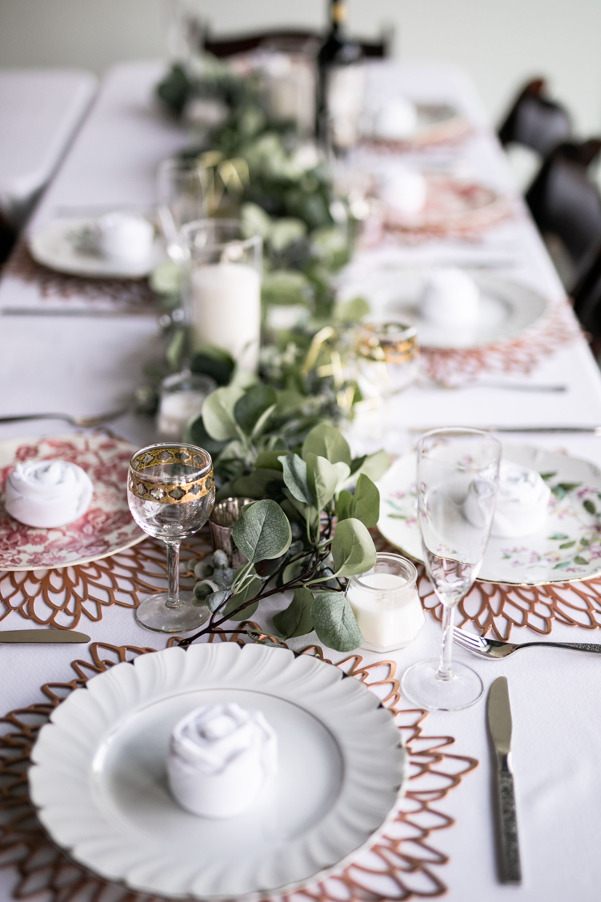 A long table with plates , glasses , utensils and a garland on it.