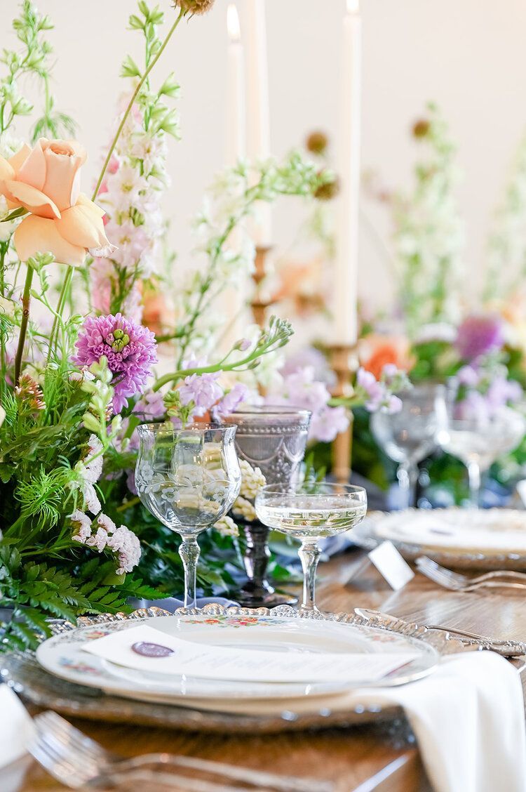 A table set for a wedding reception with plates , glasses , candles and flowers.
