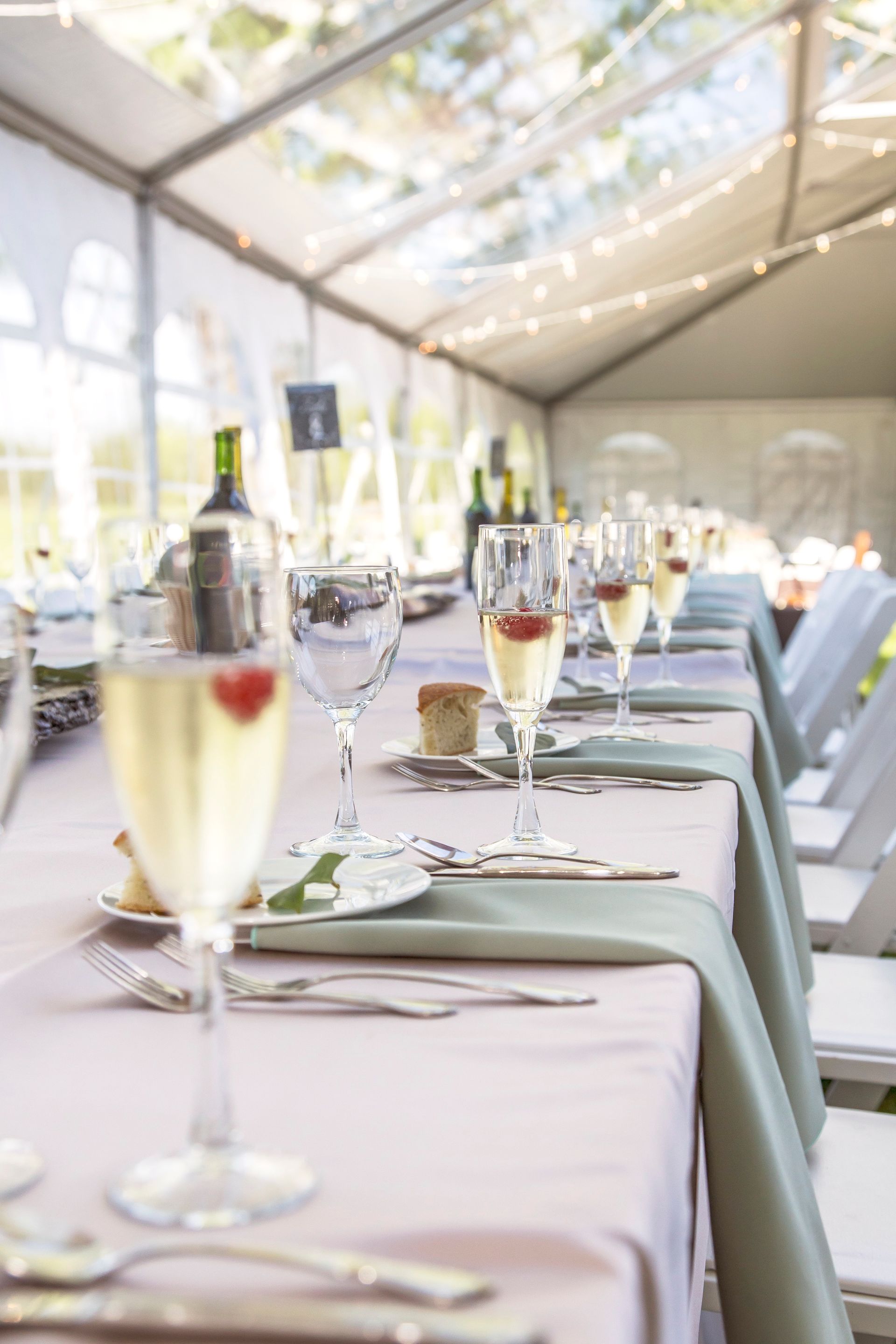 A long table set for a wedding reception with glasses of champagne and strawberries on it.