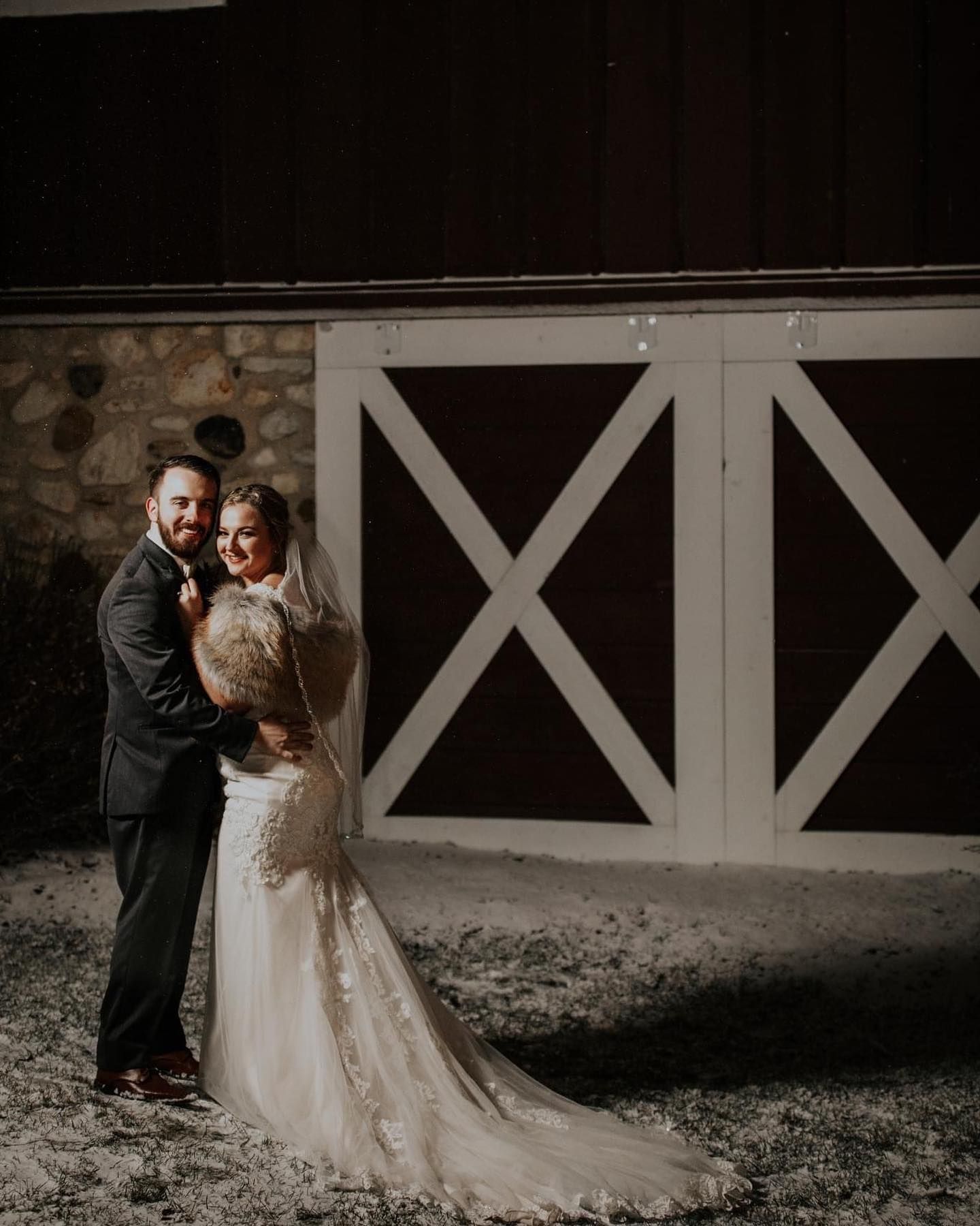 A bride and groom are posing for a picture in front of a barn.