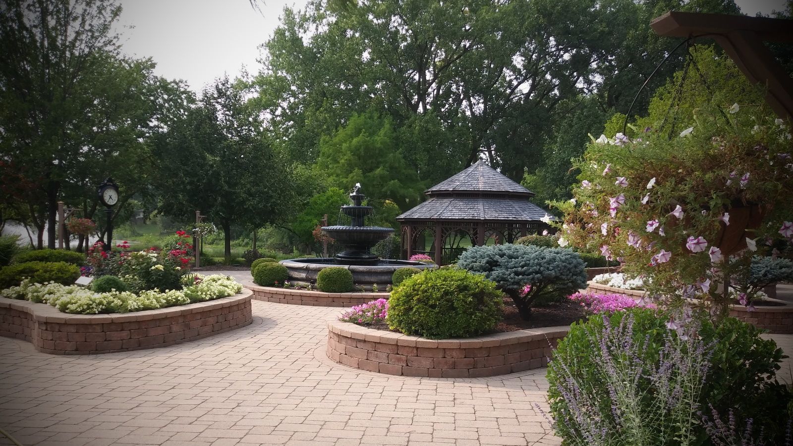 There is a gazebo in the middle of a garden with a fountain.