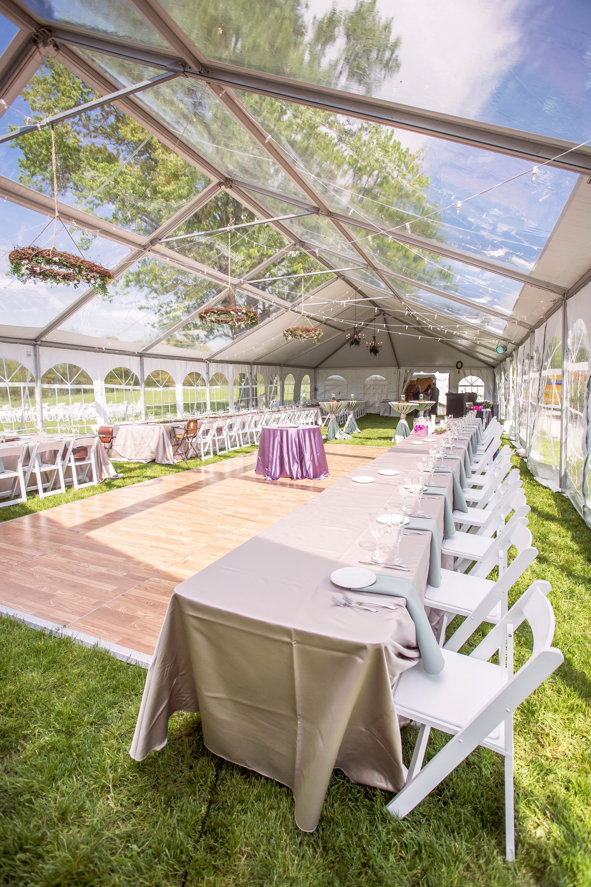 A clear tent with tables and chairs set up for a wedding reception.