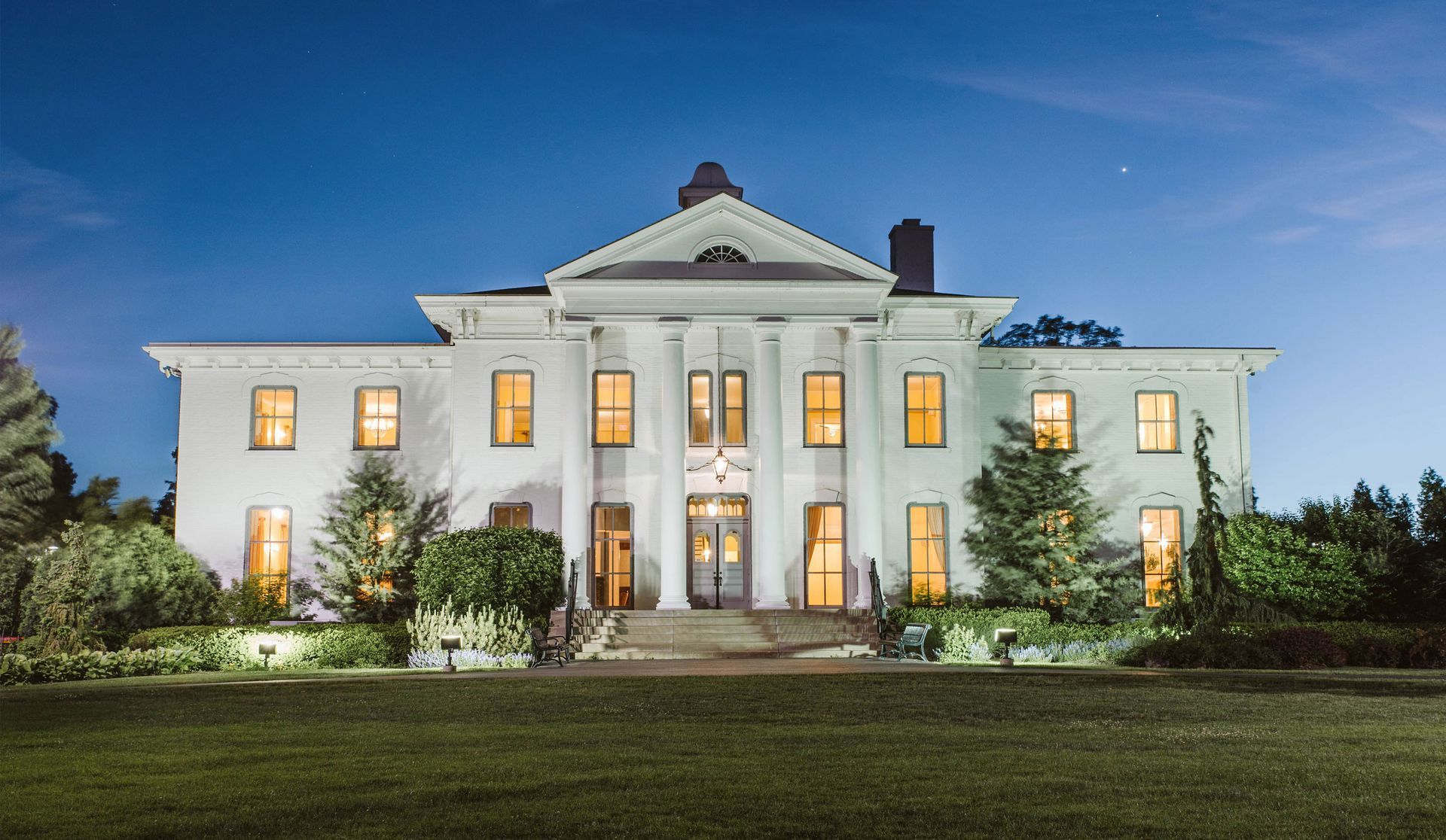 A large white house with lots of windows is lit up at night