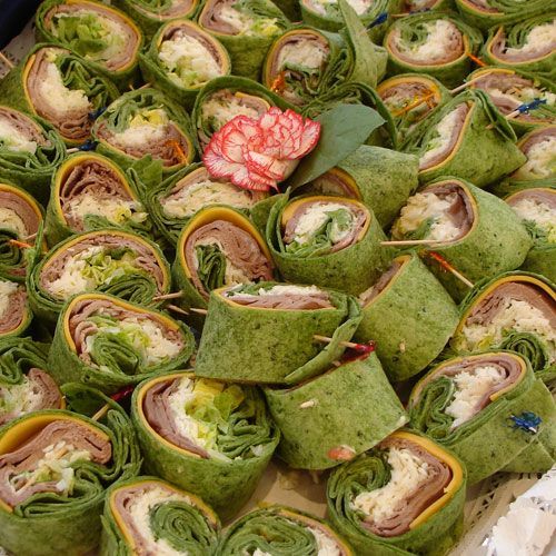 A bunch of green wraps with meat and cheese on a table.