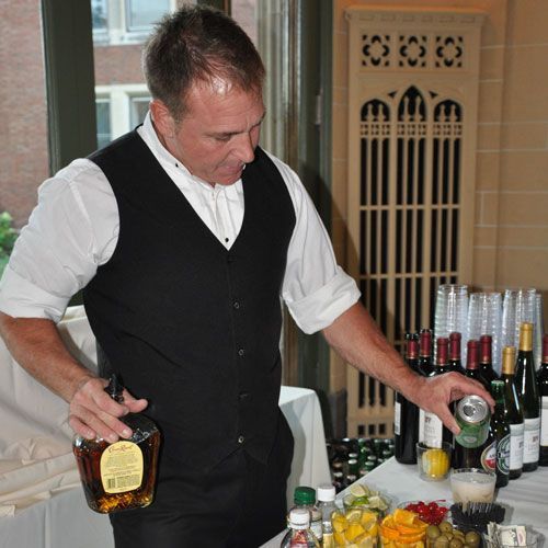 A man in a black vest is pouring a drink into a glass