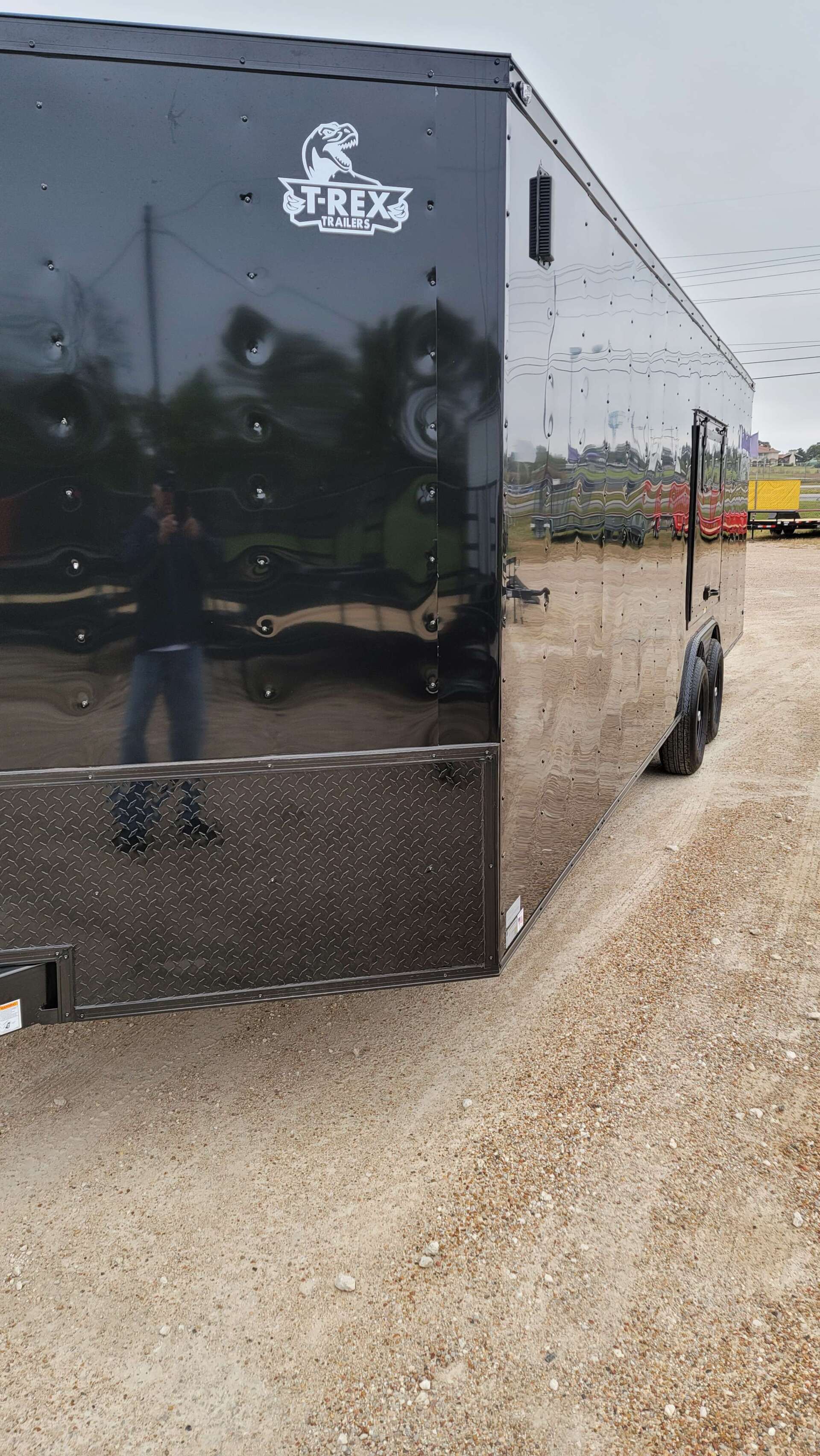 A black trailer is parked in a gravel lot.