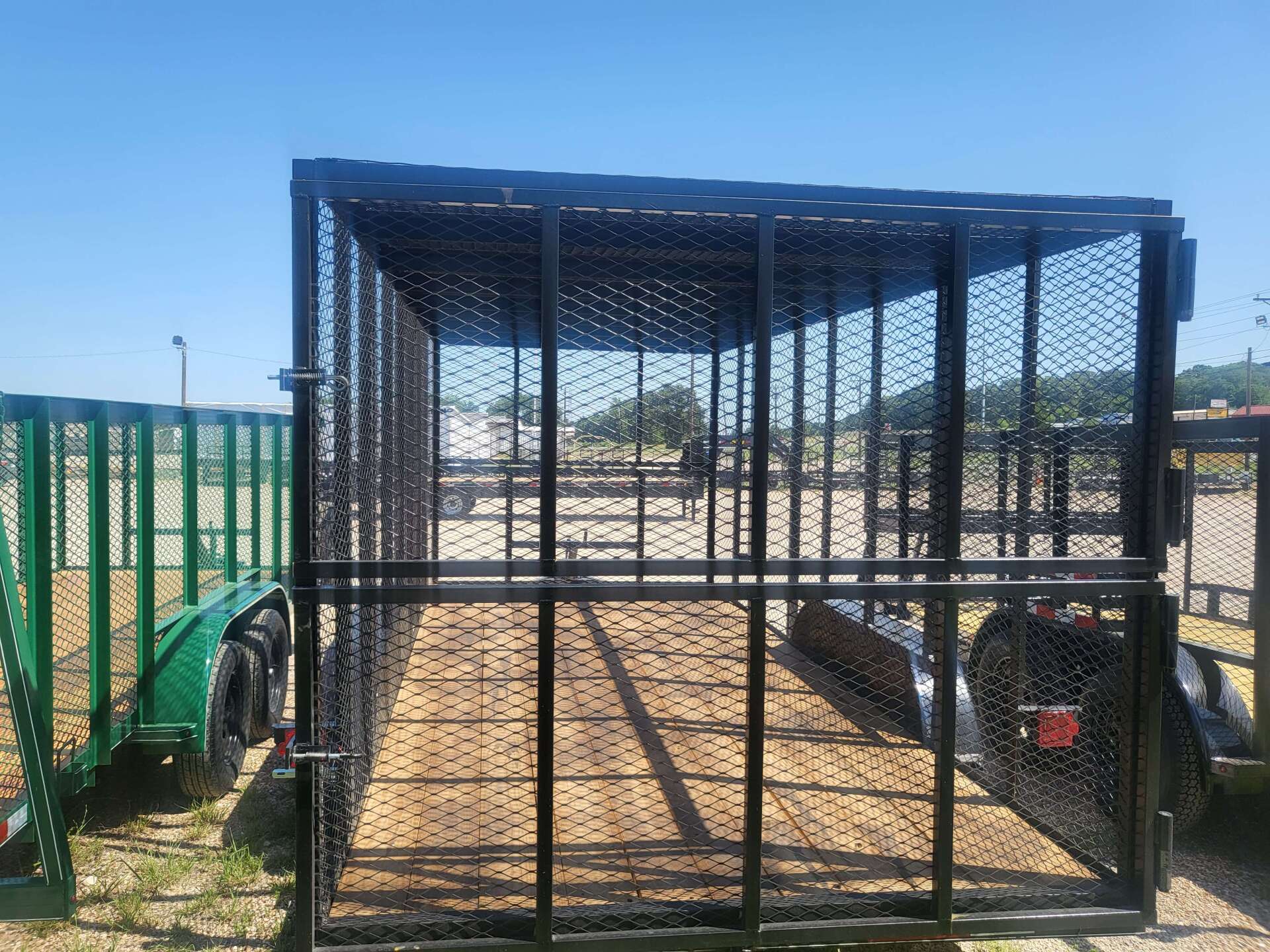 A green trailer is parked next to a black cage.