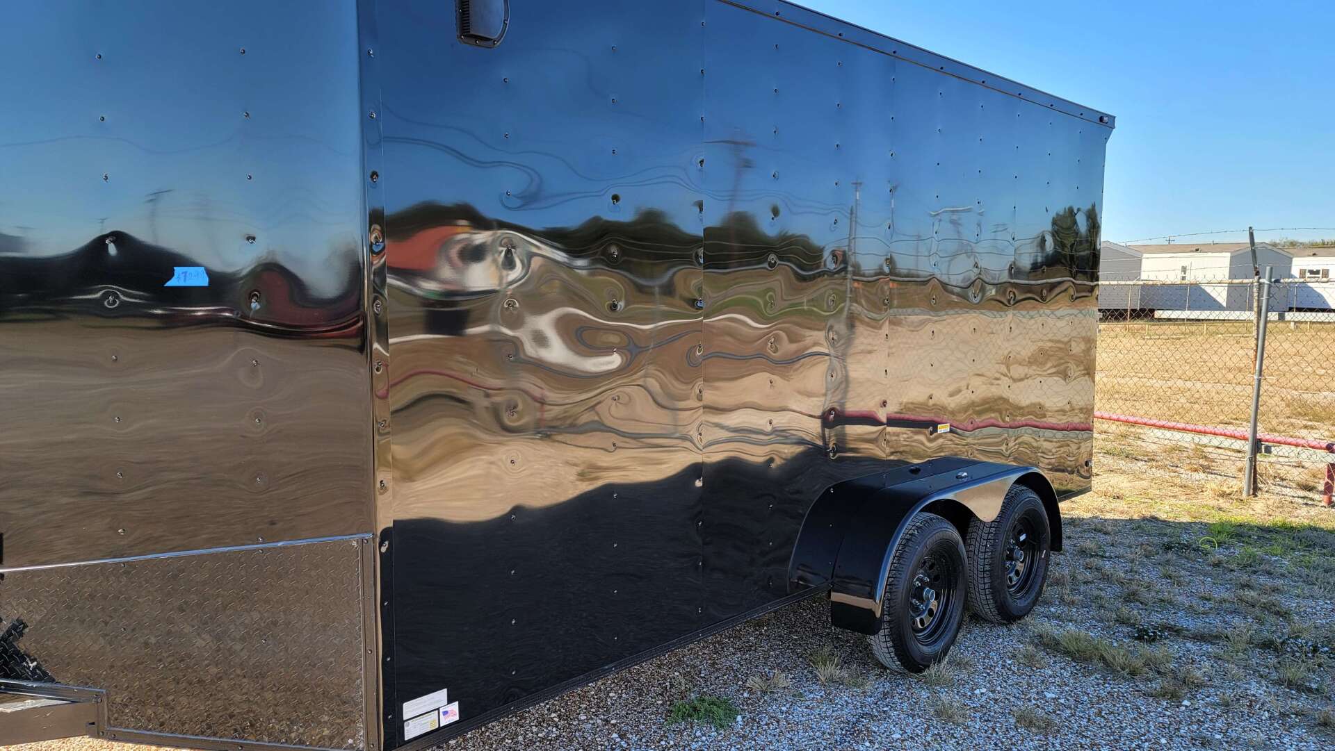 A black trailer is parked in a gravel lot.