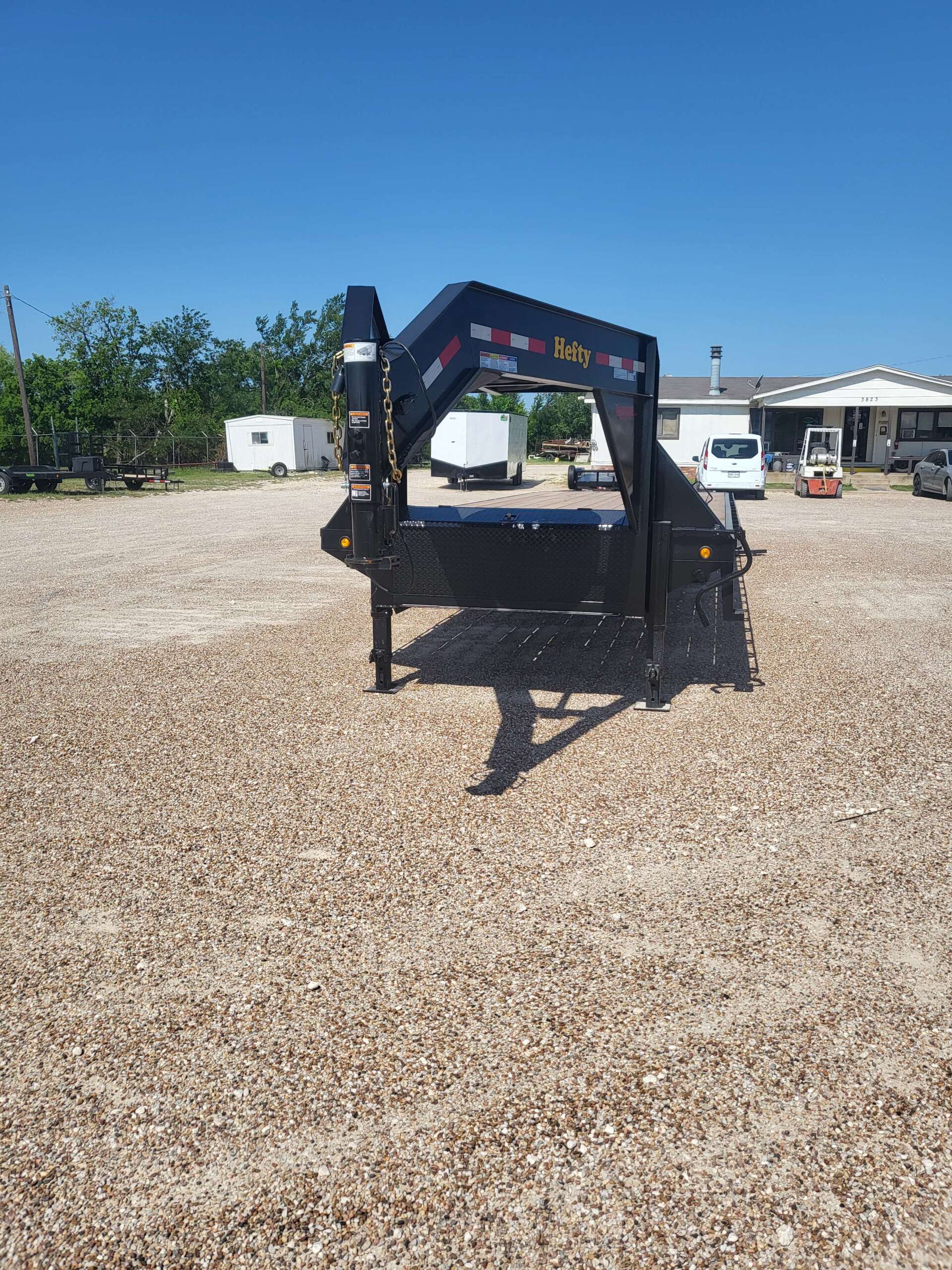 A trailer is parked in a gravel lot in front of a house.