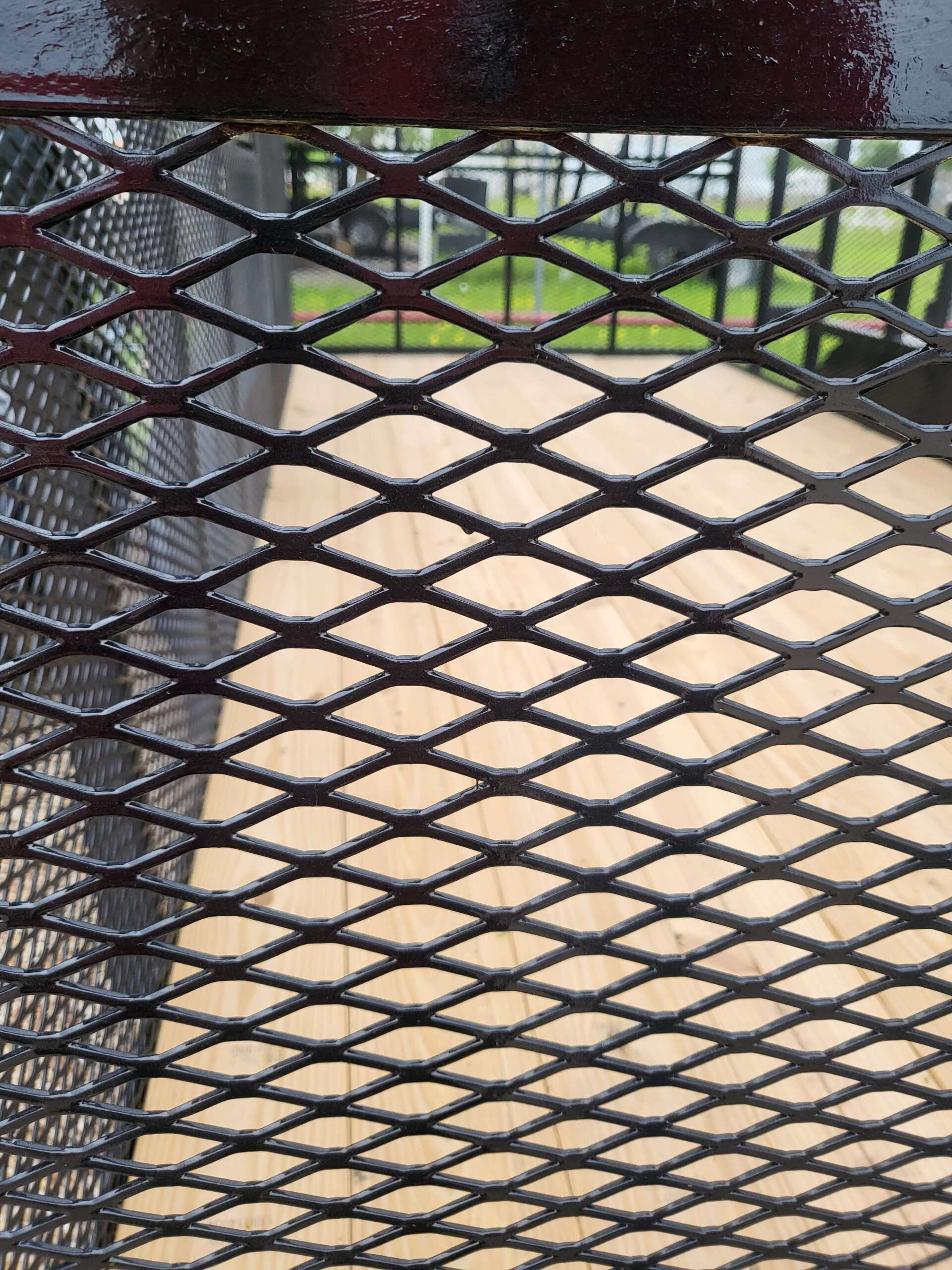 A close up of a metal fence with a wooden deck in the background