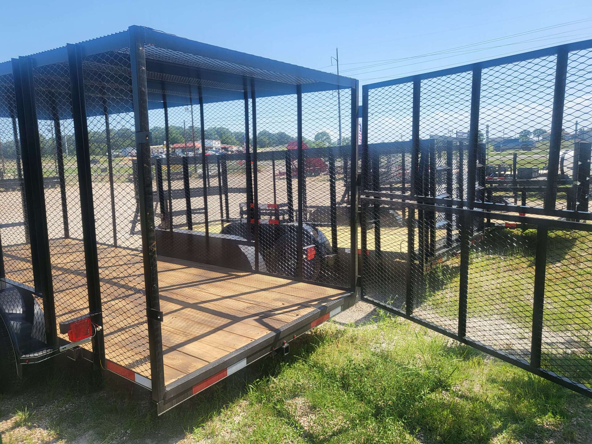 A trailer with a cage on top of it is parked in a grassy field.