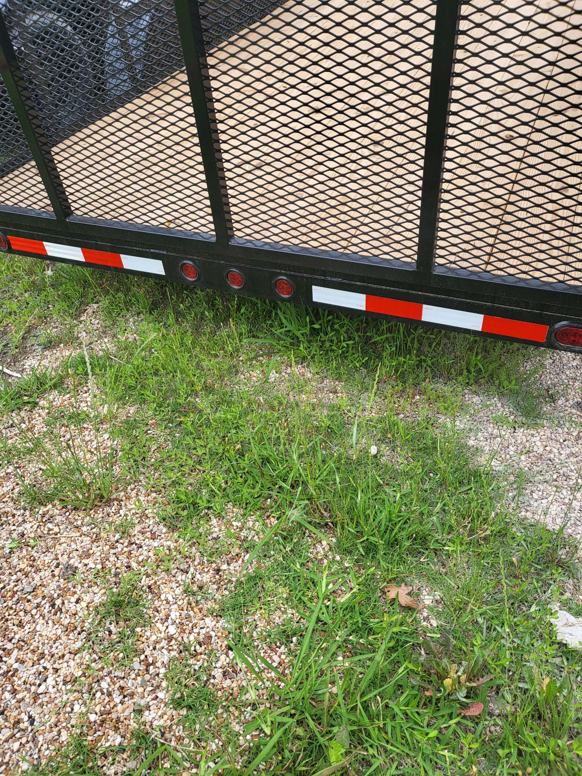 A trailer is parked in the grass next to a gravel road.