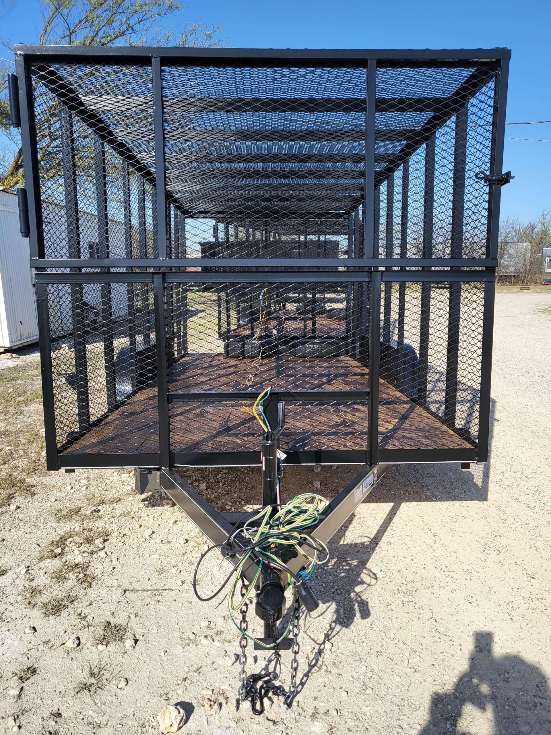 A trailer with a cage attached to it is sitting on top of a dirt field.