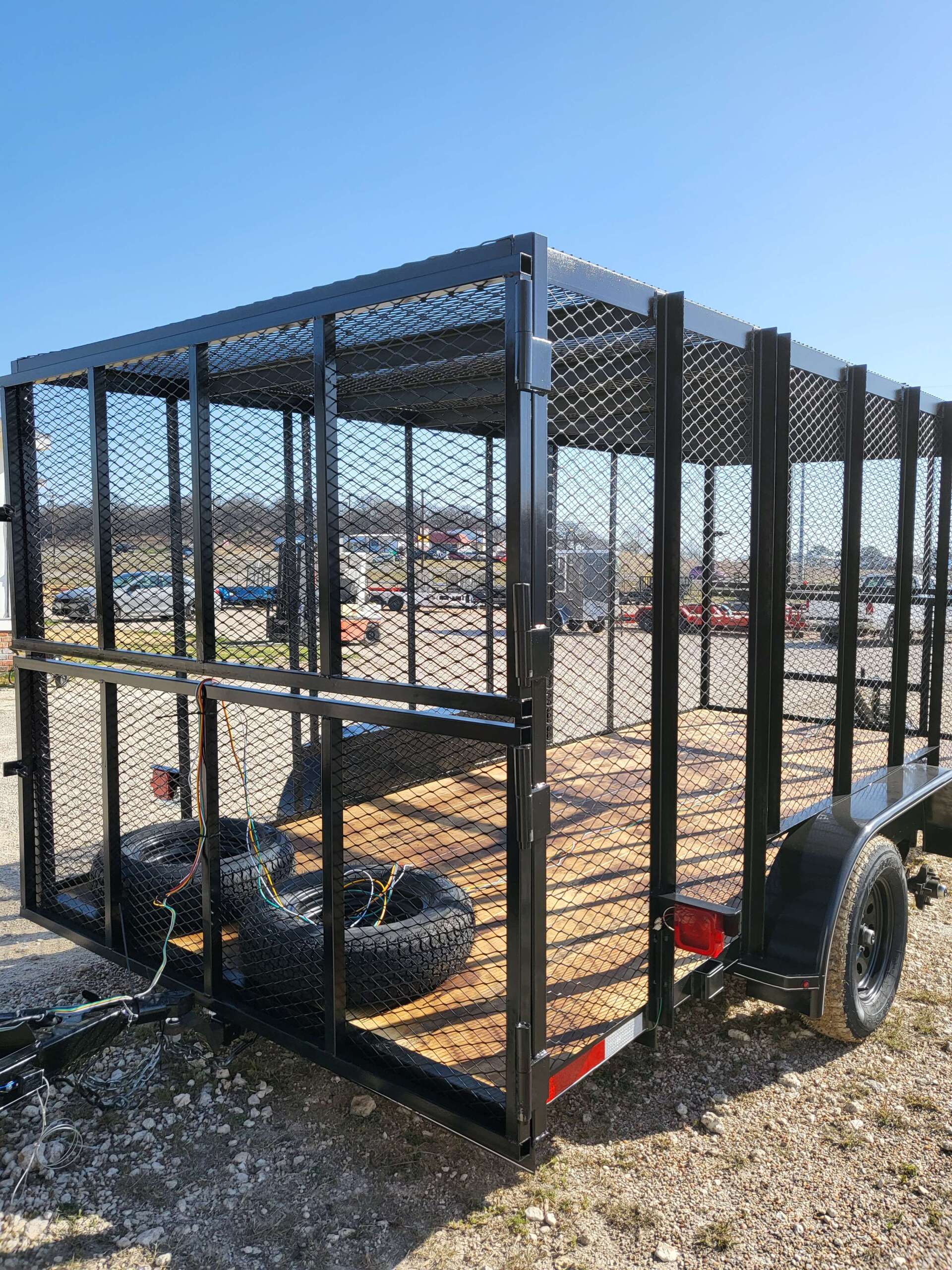 A trailer with a cage attached to it is parked in a gravel lot.