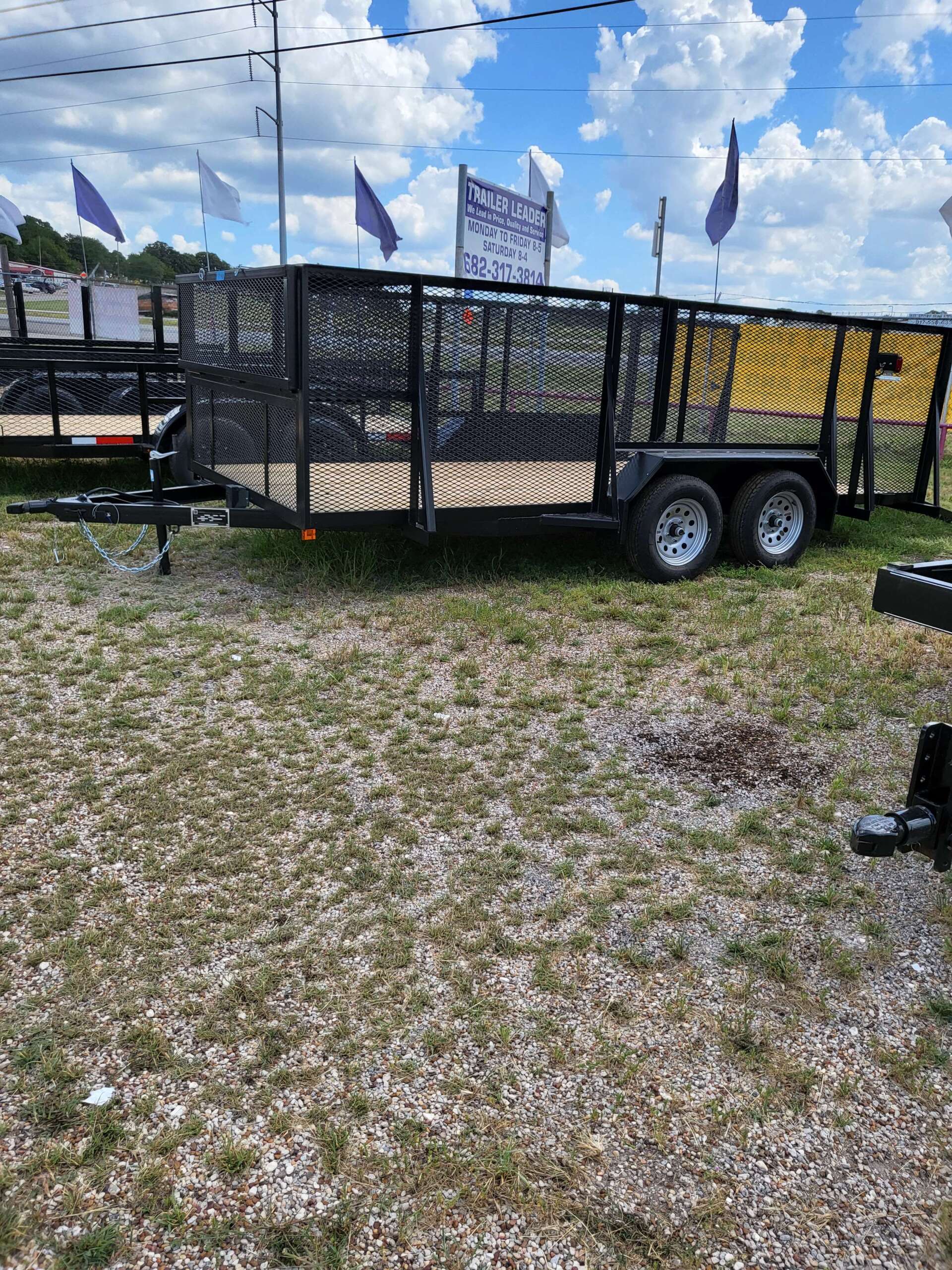 A trailer is parked in the grass in a gravel lot.