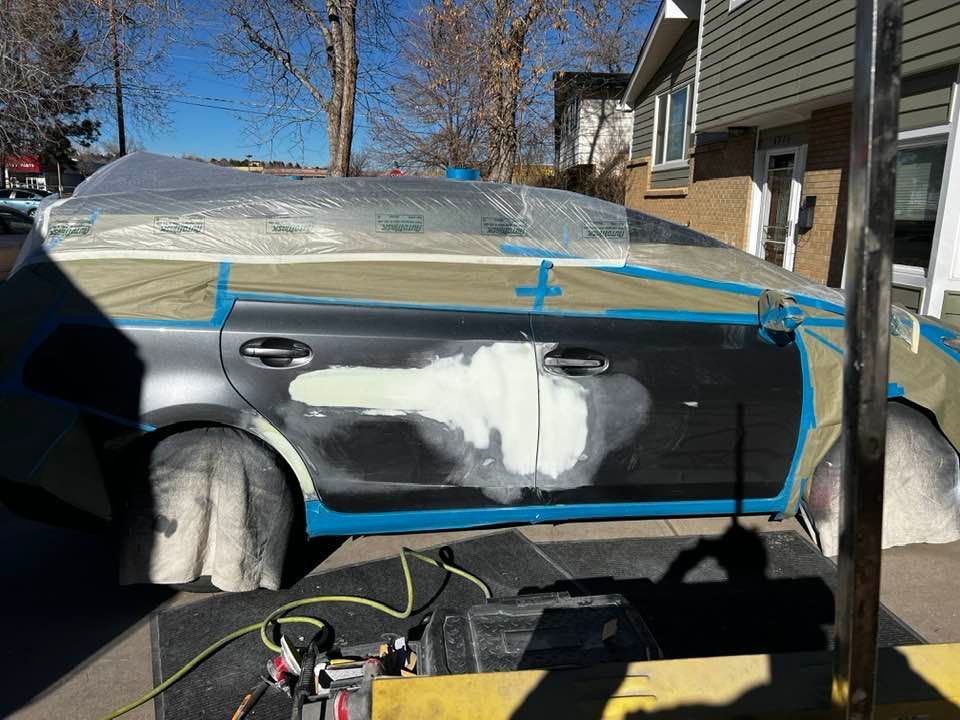 A car is being painted in a driveway in front of a house.
