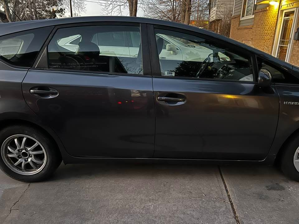 A black prius is parked in a driveway in front of a house.
