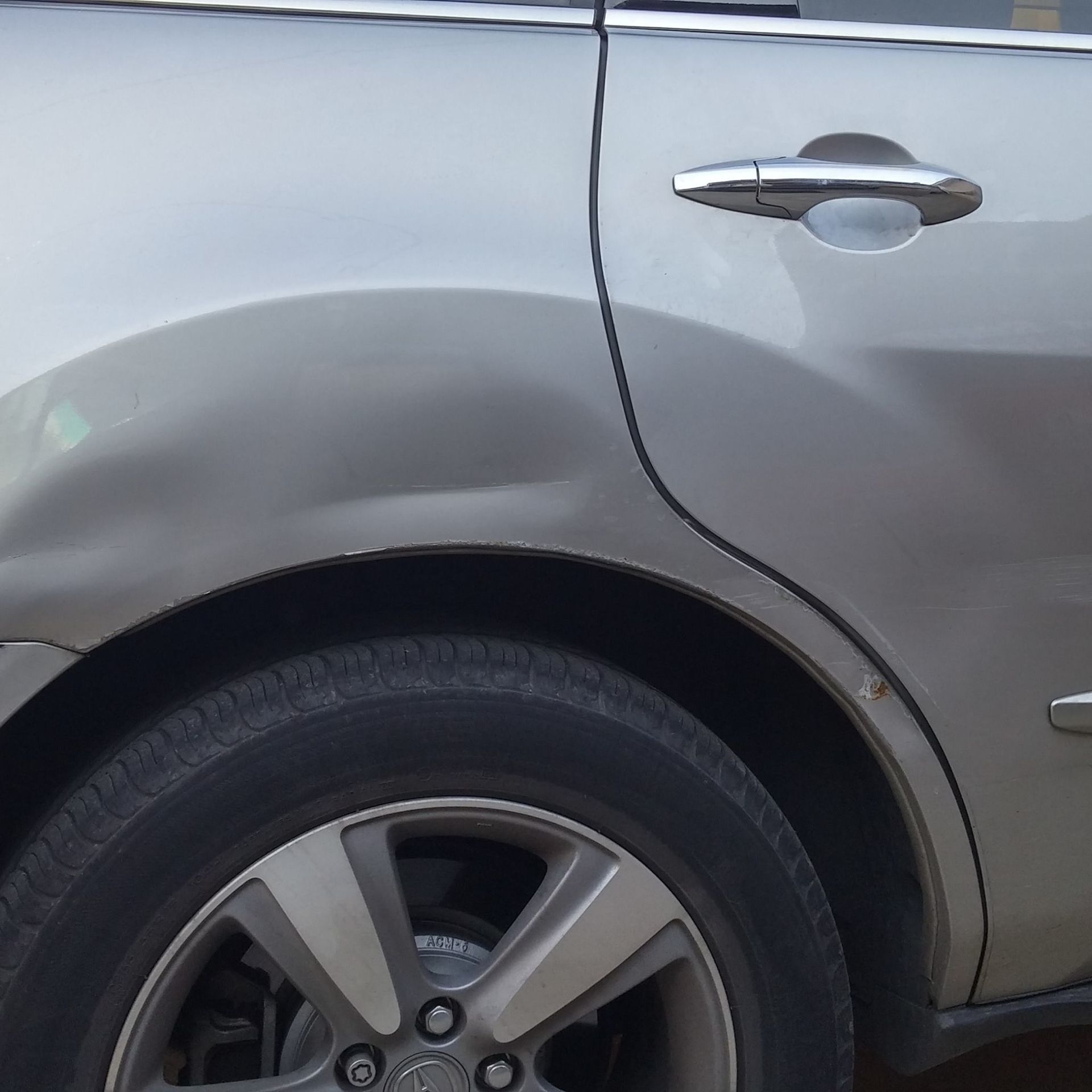 A silver car with a damaged fender and a black tire