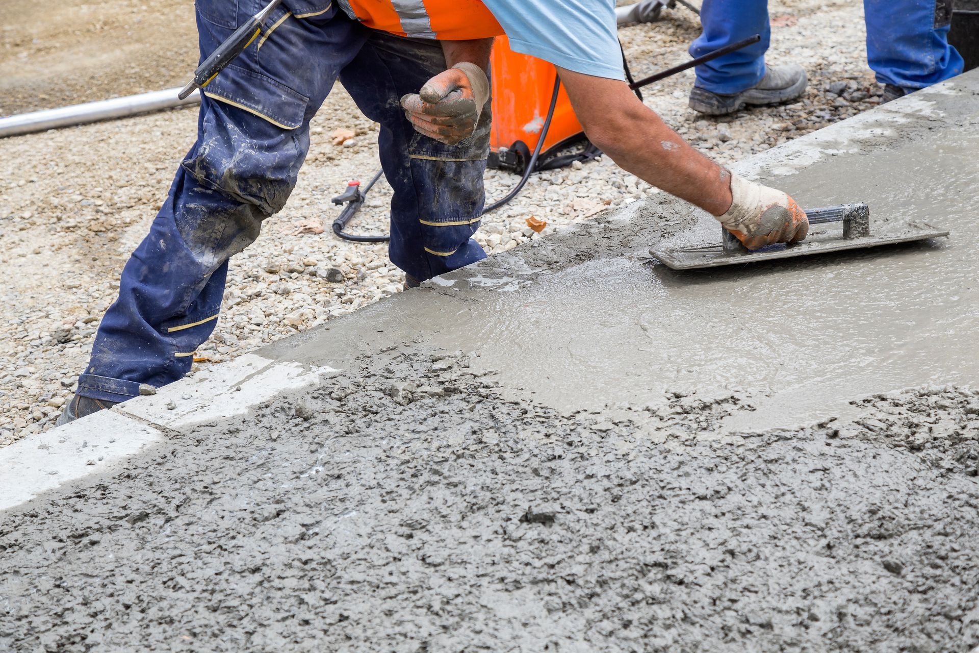 A worker smooths fresh concrete with a trowel, creating a durable surface.