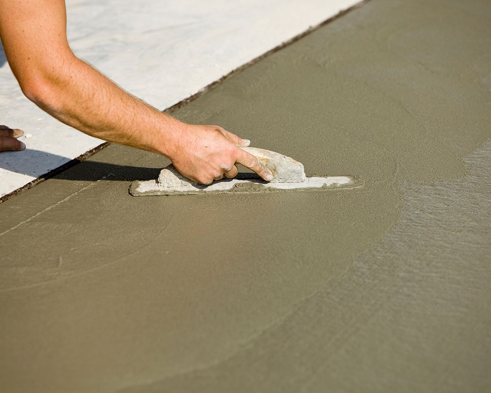 Worker smoothing a driveway with a concrete trowel, showcasing professional concrete construction se