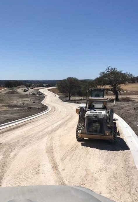 A construction site with a yellow bulldozer smoothing out a winding gravel road under a blue sky.