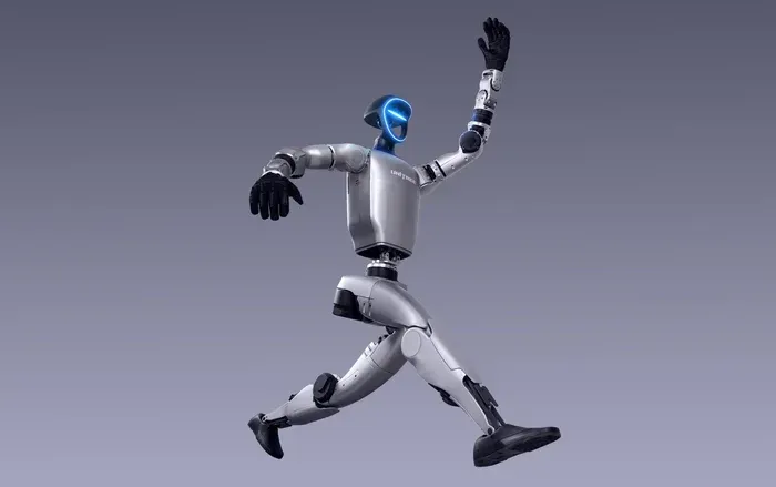 Bipedal robot with teal torso, black limbs, and silver lower legs stands against a cloudy sky.