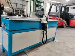 Máquina industrial azul y blanca con una manguera negra; una carretilla elevadora roja en el fondo.