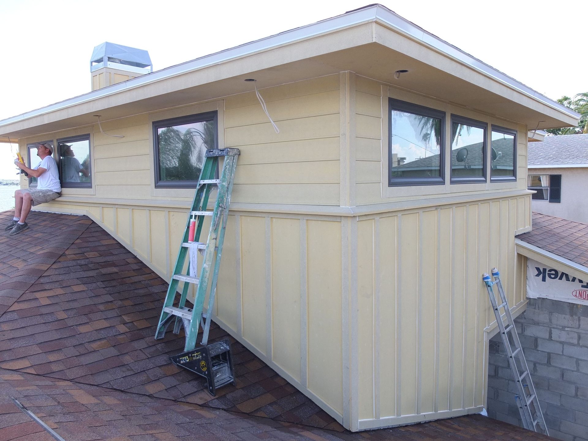 A man is sitting on the roof of a house with a ladder attached to it.