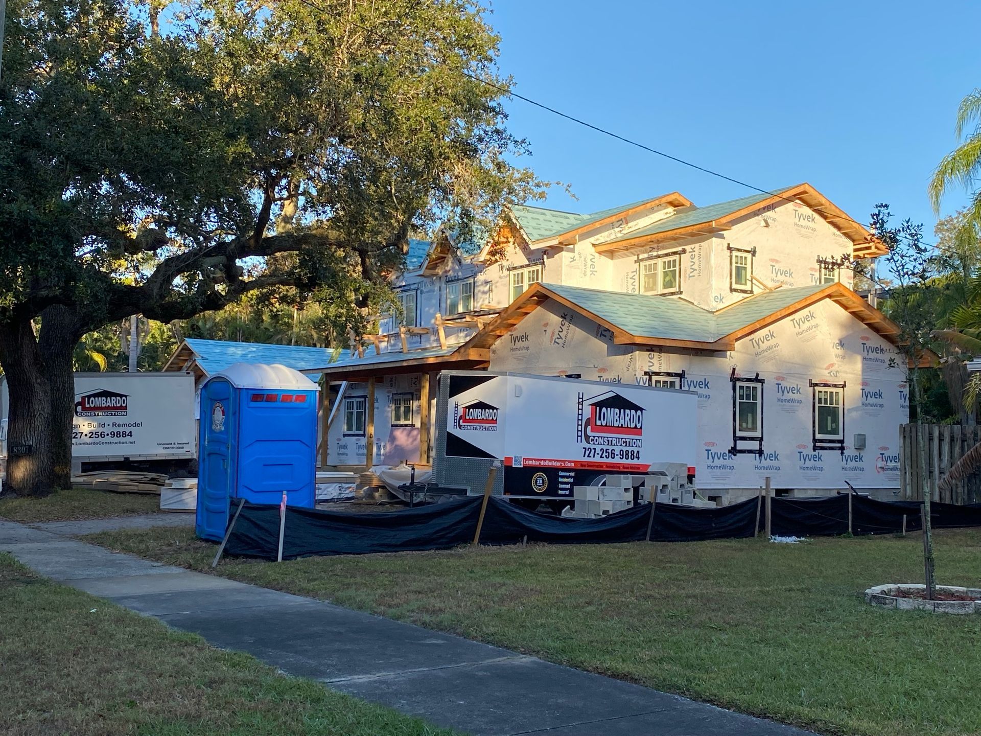 A house is being built in a neighborhood with a blue portable toilet in front of it.
