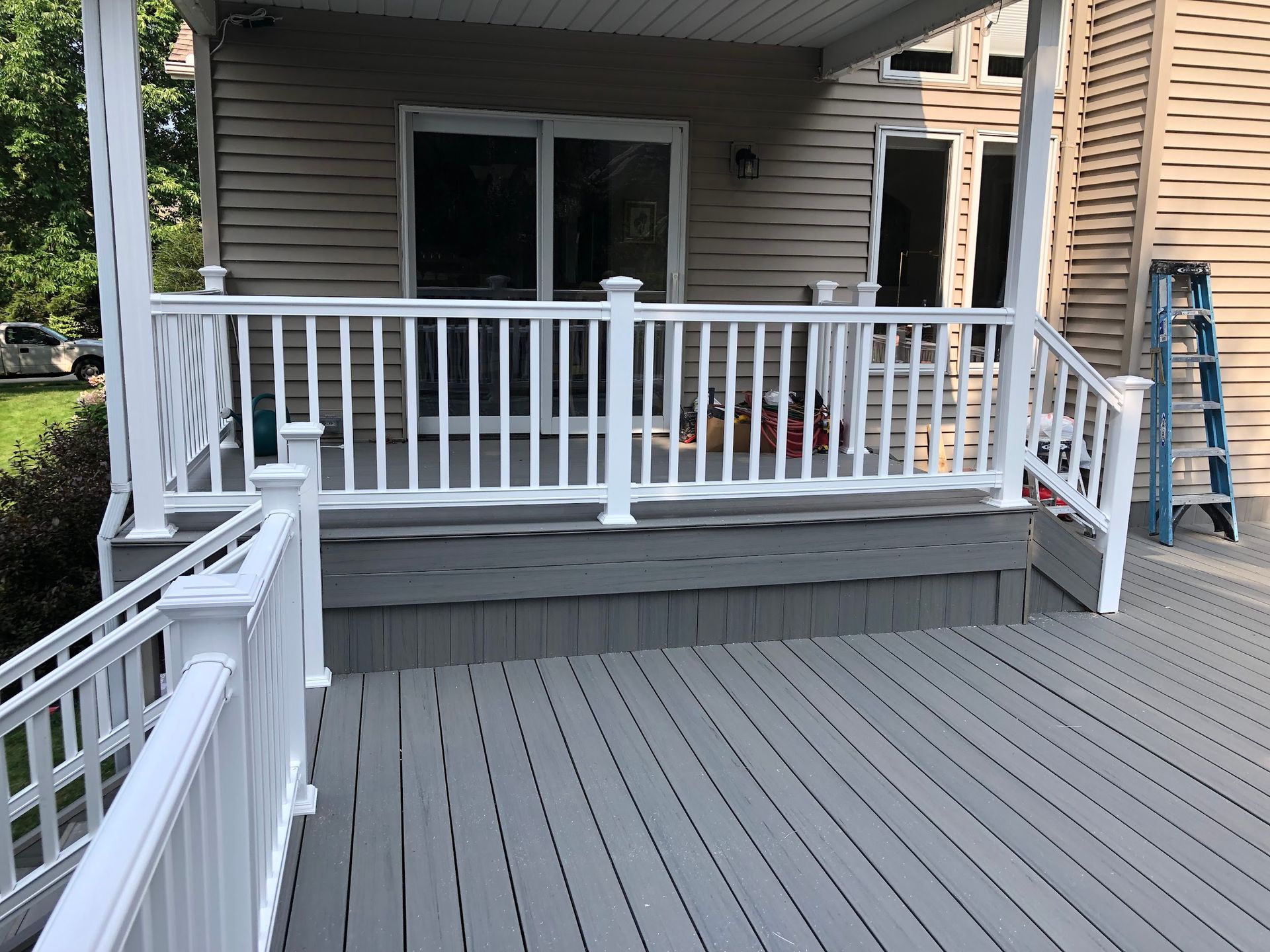 A deck with a white railing and a ladder in front of a house.