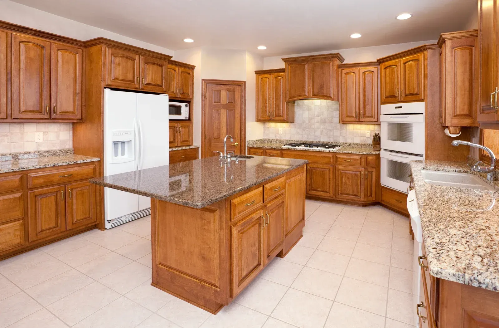 Kitchen with brown cabinets, granite countertops, and a central island. White appliances and tile floor.